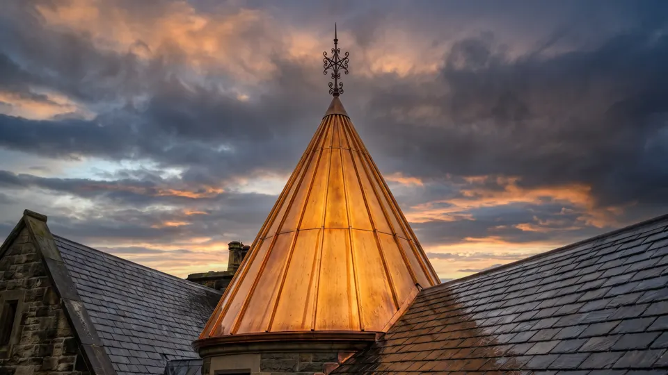 A copper-clad turret in full golden light above falling slate planes